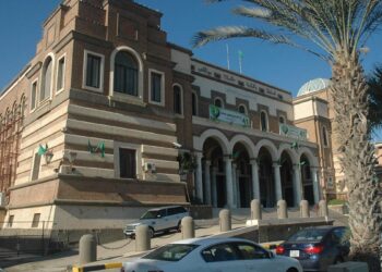 مبنى المقر الرئيسي لمصرف ليبيا المركزي في طرابلس تتقدمه أشجار النخيل وسيارات متوقفة